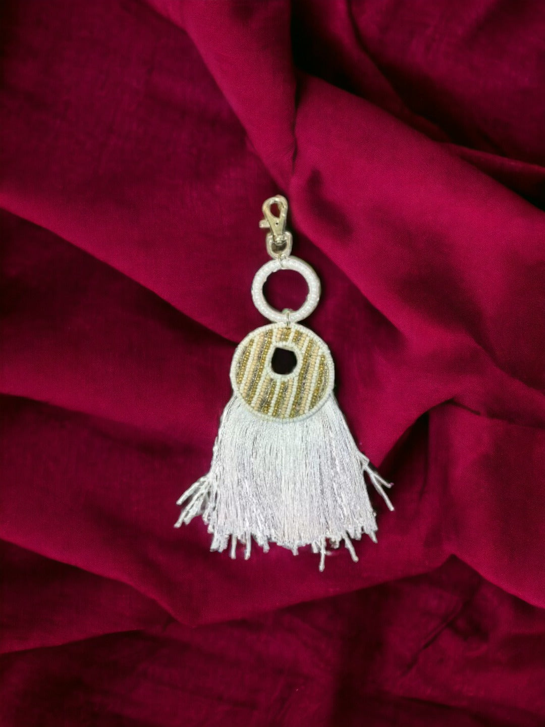 A Vdesi White tassel bag charm on  plain red sheet.